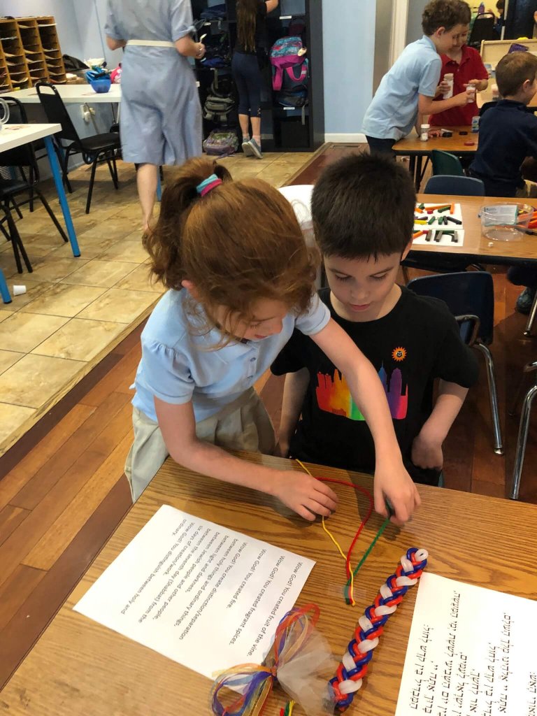 Children practice braiding yarn at a table with Havdallah supplies.