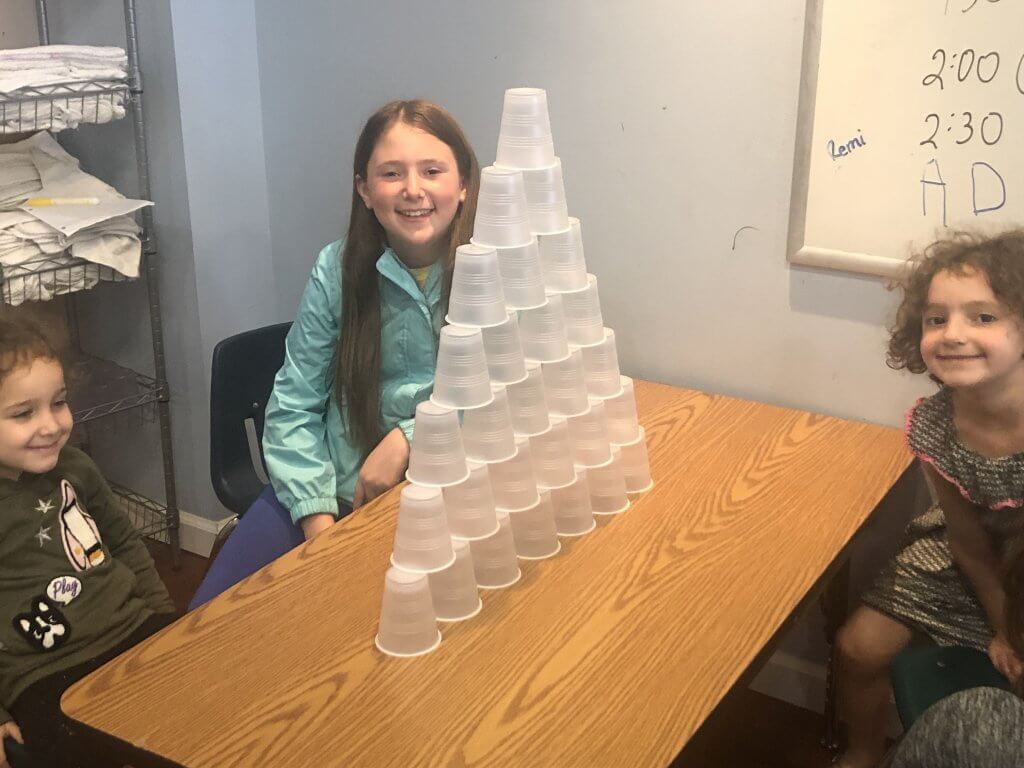 Three kiddos sitting next to a tall pyramid of plastic cups.