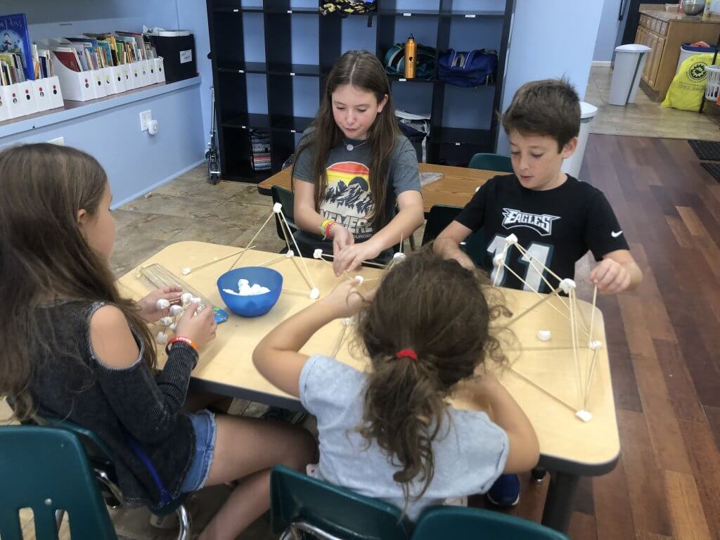 Four children building towers out of marshmallows and skewers.