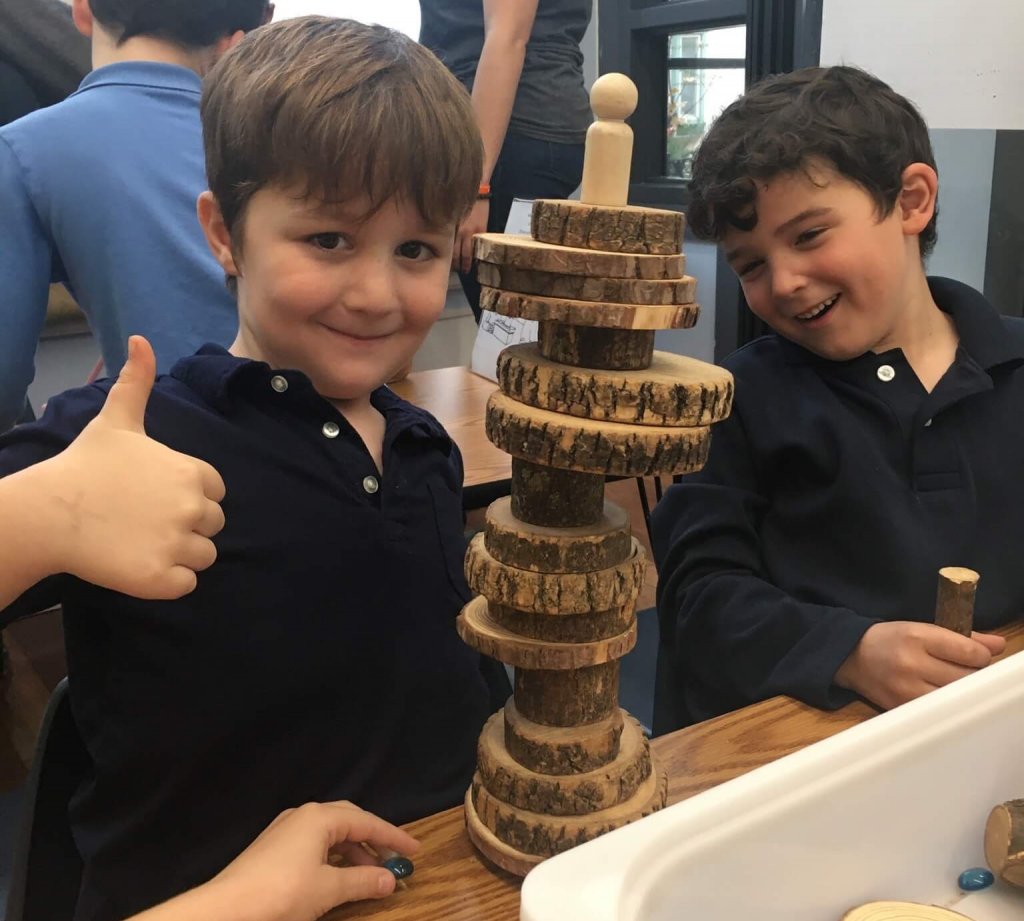 Two students show off the tower they built out of natural materials.