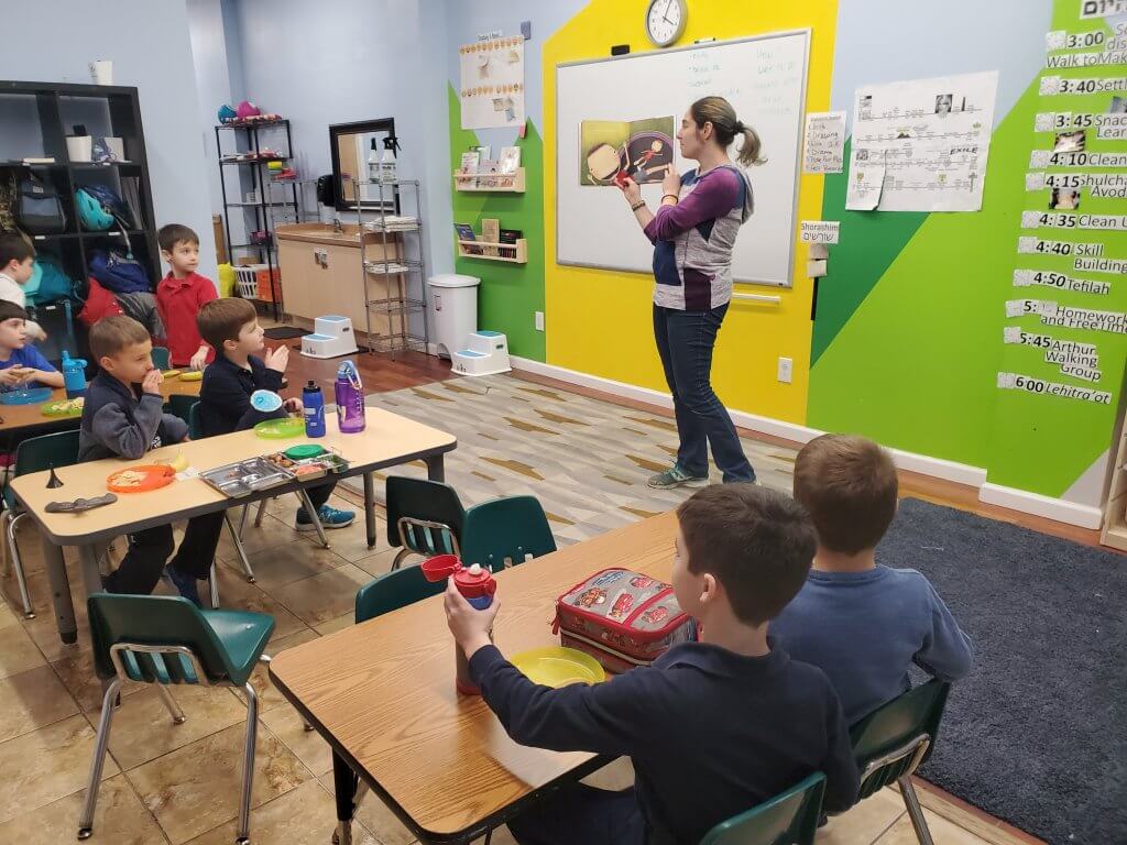 Gaby reads a book to the shorashim (1st grade) kiddos over snack.