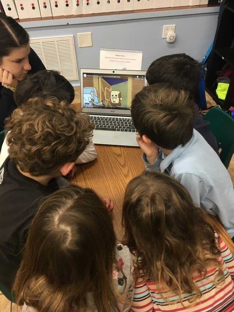 Isabella and a group of students crowd around a computer to watch an animated version of the story from our text.