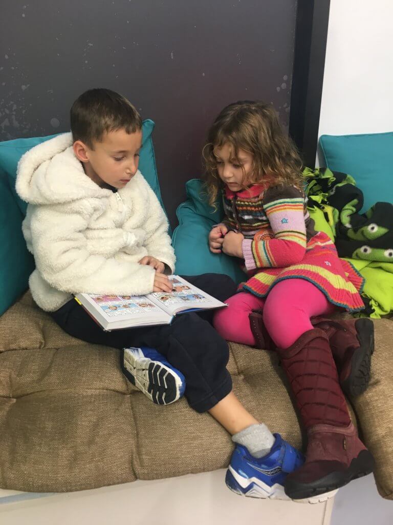 A 1st grader cozies up with a PreK kid to read on the windowsill.