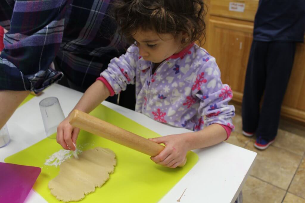 A pre-K kiddo rolls out dough for Hamantaschen.